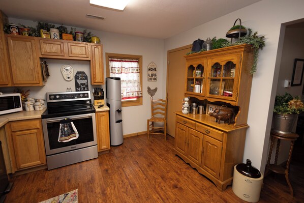 A kitchen with wooden cabinets, a stainless steel stove, a refrigerator, and a window with a curtain.