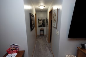 A narrow hallway with a carpeted floor, framed artwork on the walls, and a door at the end.