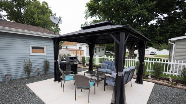 Une terrasse couverte, aménagée avec du mobilier d’extérieur, un barbecue et une antenne parabolique.
