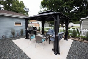 A covered patio with outdoor furniture, a grill, and a satellite dish.