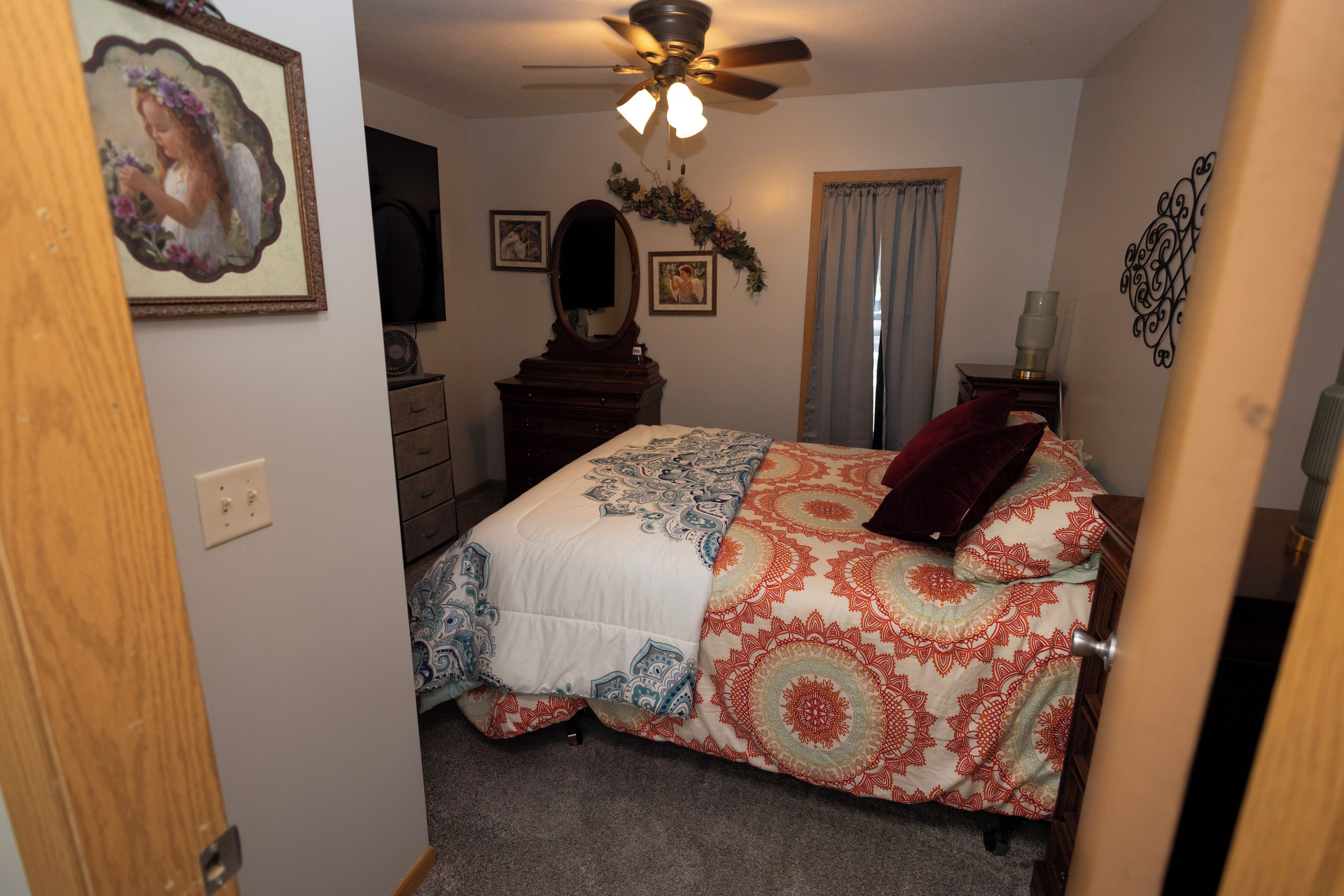 Quarto com cama, penteadeira, espelho, ventilador de teto e detalhes decorativos nas paredes.