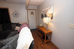 A room with a bed, a wooden table with a lamp, a door with a sign, and a wall decoration.