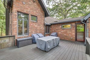 Een overdekt terras buiten, met een bakstenen muur, een schuifpui en een houten terras.