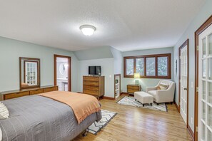 Een slaapkamer met een bed, dressoir, televisie, stoel en een raam met zonwering.