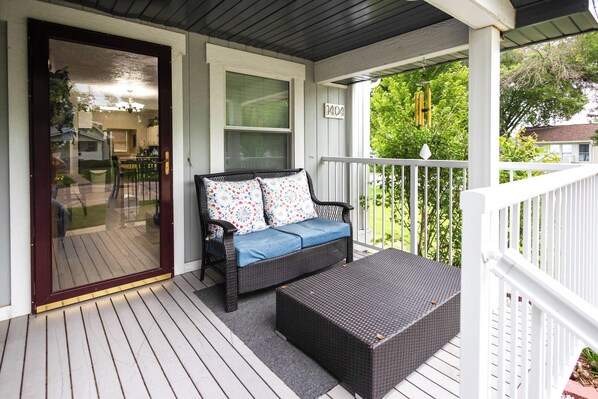 A covered porch with a wicker sofa, a small table, and a view of the backyard.
