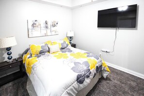 A bedroom with a bed, a TV mounted on the wall, and a nightstand with a lamp.