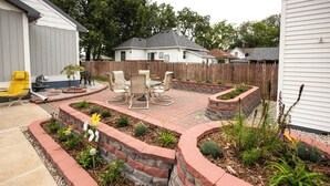 Un jardin à l’arrière de la maison, avec une terrasse, du mobilier d’extérieur et un espace planté de différentes espèces végétales.