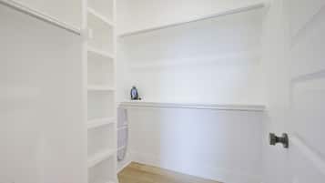 Un armario blanco con estantes fijos, barra para colgar ropa y un tendedero de metal.