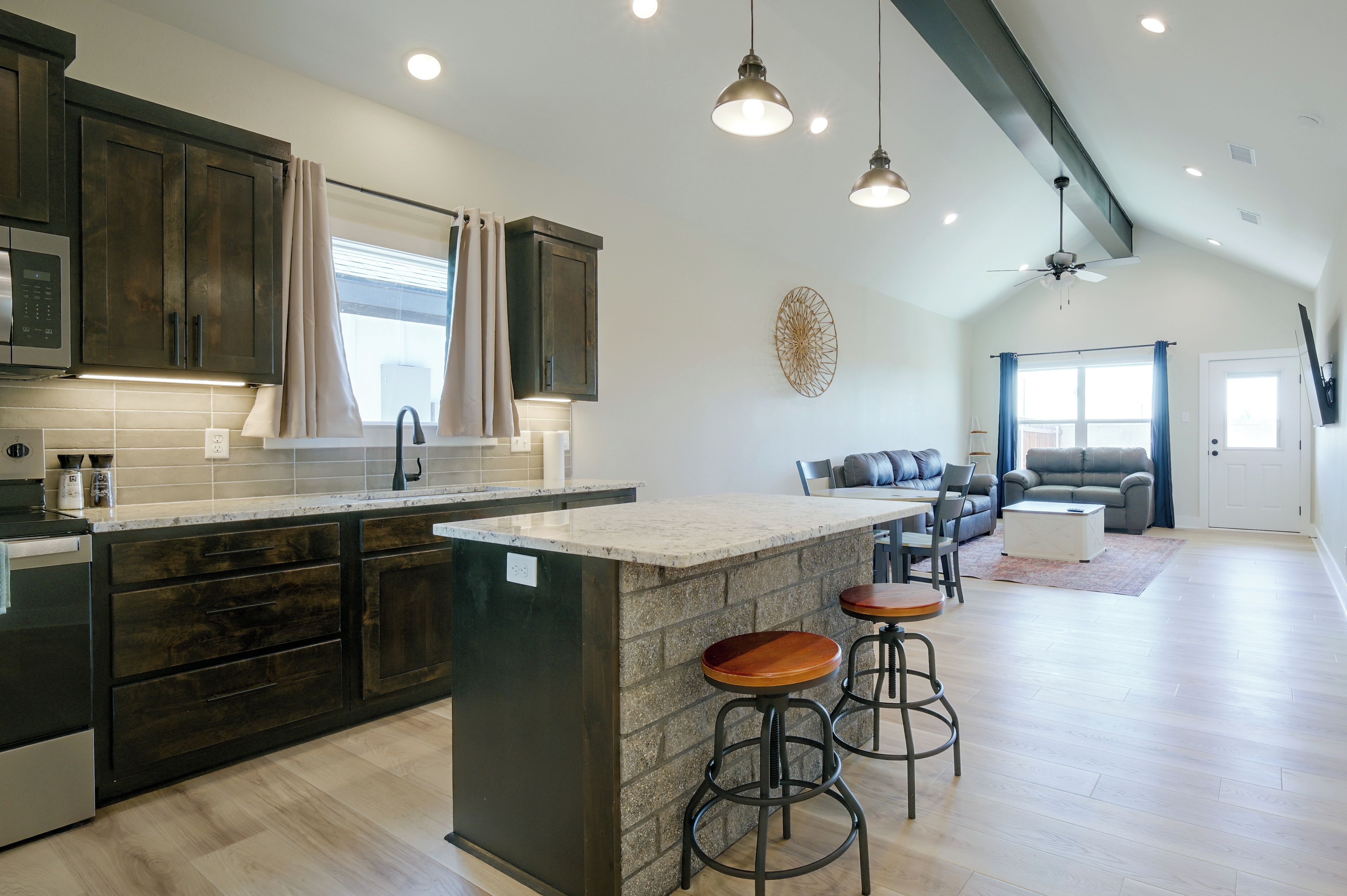 Una cocina moderna con armarios oscuros, una isla central con taburetes y un comedor con sofá y sillas.