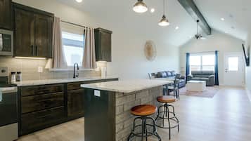 Una cocina moderna con armarios oscuros, una isla central con taburetes y un comedor con sofá y sillas.