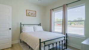Una habitación con cama, ventana con cortinas, una puerta y un cuadro en la pared.