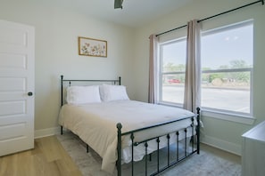 Ein Zimmer mit einem Bett, einem Vorhangfenster, einer Tür und einem gerahmten Bild an der Wand.