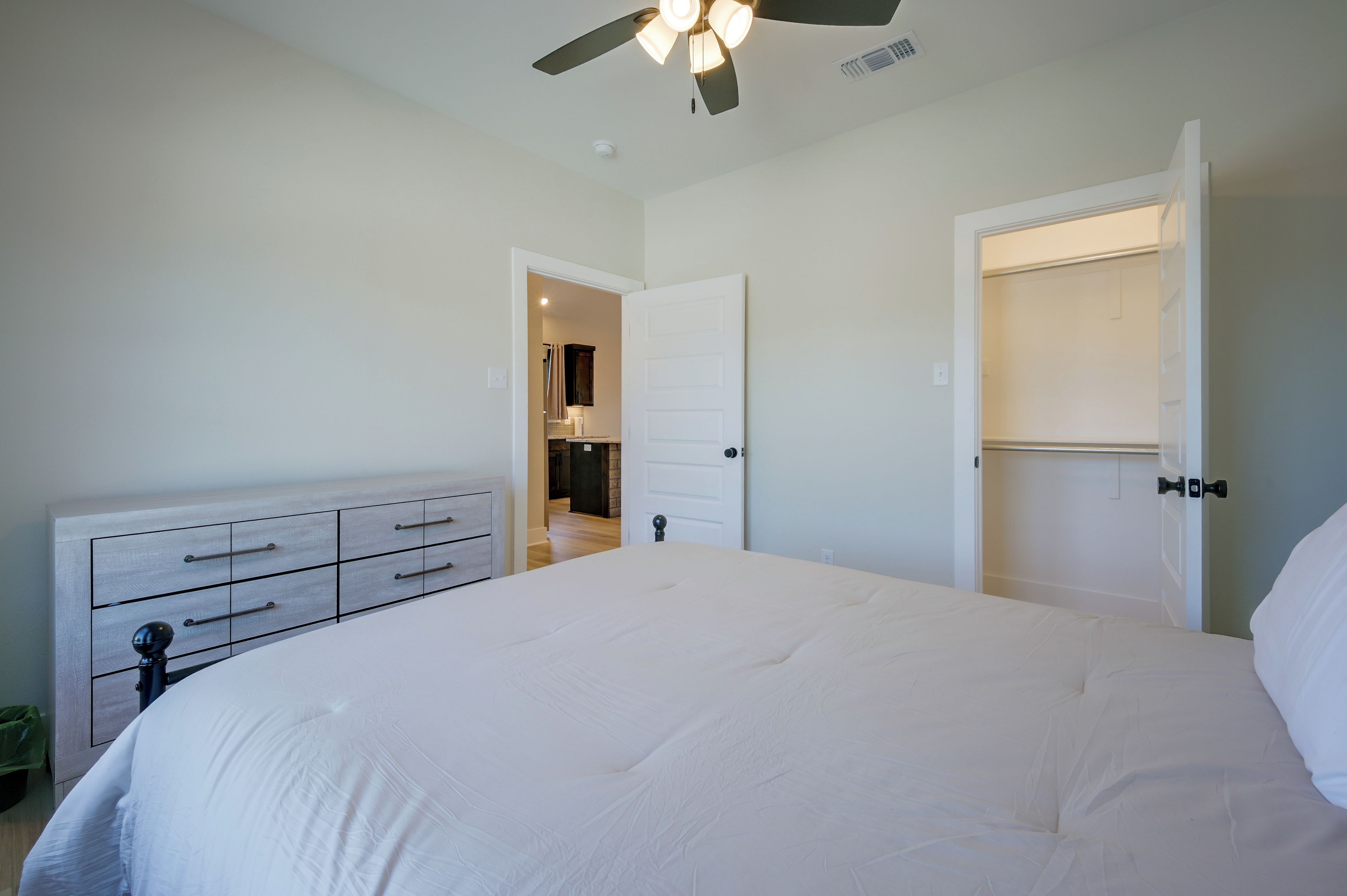 Un dormitorio con cama, cómoda, armario y baño visible a través de una puerta abierta.