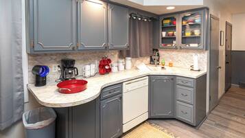 A compact kitchen with grey cabinets, a dishwasher, a coffee maker, and a red bowl on the counter.