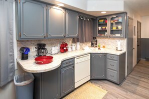 A compact kitchen with grey cabinets, a dishwasher, a coffee maker, and a red bowl on the counter.