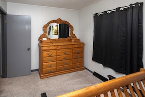 A bedroom with a wooden dresser, a mirror, a black curtain, and a door.