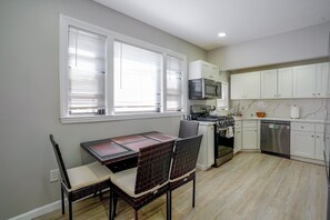 A kitchen with white cabinets, a microwave, stove, and dishwasher. There is a dining table with chairs. - Boston Basecamp: Modern Malden Apartment (Malden)