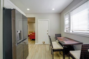 A compact kitchen with a refrigerator, a dining table with chairs, and a window with blinds. - Boston Basecamp: Modern Malden Apartment (Malden)