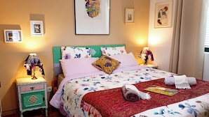Un llit ben fet amb roba de llit floral, una tauleta de nit verda amb una làmpada, i un quadre al mur.