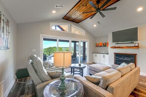 Un salon comprenant un canapé, une table avec une lampe, un ventilateur de plafond et un téléviseur fixé au mur.