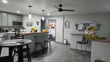 Cozinha moderna com micro-ondas, fogão e área de refeições com cadeiras e mesa.