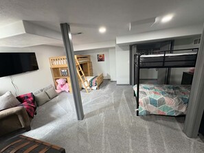 Un dormitorio con literas, un sofá, un televisor y una casita de juegos de madera.