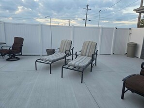 Un patio con dos sillones, una mesita y un bote de basura.