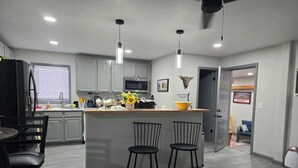 A modern kitchen with a central island, bar stools, and a dining area with a table and chairs. - 'Honey Bee' Family Home in Columbus, Nebraska! (Columbus)
