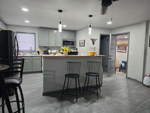 Una cocina moderna con una isla central, taburetes de bar y una zona de comedor con mesa y sillas.