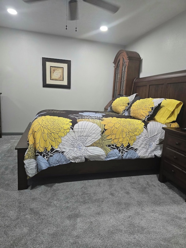Une chambre à coucher comprenant un lit, une commode, une armoire, un ventilateur de plafond et un certificat encadré accroché au mur.