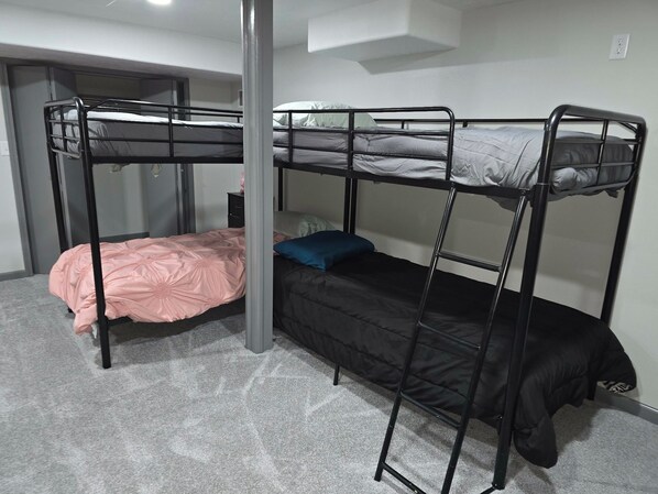 Habitación con literas, alfombra gris, pared blanca y una puerta al fondo.