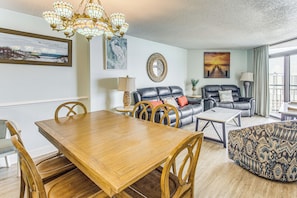 A living room with a wooden dining table, a sofa, a patterned armchair, and a chandelier. - Sand Dunes Resort Condo w/ Water Views! (Myrtle Beach)