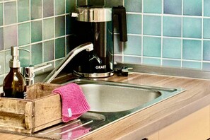 Una cocina con un lavamanos de acero inoxidable, una cafetera y una botella de jabón para manos.