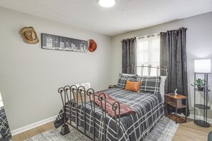 Un dormitorio con cama, mesita de noche, lámpara, ventana con cortinas y una obra de arte con un paisaje urbano en la pared.