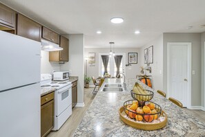 Una cocina con una isla central, electrodomésticos blancos y un comedor con vista al salón.