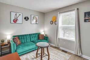 A living room with a teal sofa, a round coffee table, and artwork on the walls. - Hands of Pearls Easy Access to 12 South Nashville (Nashville)