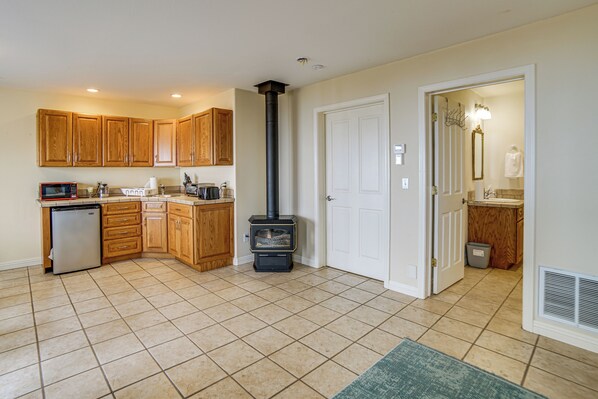 A kitchen with wooden cabinets, a built-in microwave, a small refrigerator, and a wood-burning stove.