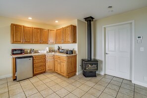 A compact kitchen with wooden cabinets, a built-in dishwasher, a microwave, a toaster, and a wood-burning stove.