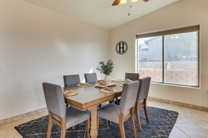 A dining area with a wooden table, grey upholstered chairs, a vase with a plant, and a large window with a view of a brick wall and trees. - Mtn Views, Hot Tub! Extended Lake Havasu Escape (Lake Havasu City)