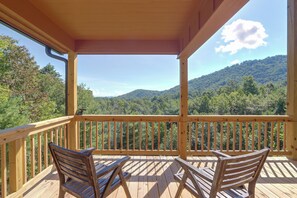 Eine Holzterrasse mit zwei Holzstühlen und einem Tisch, mit Blick auf ein bewaldetes Gebirge.