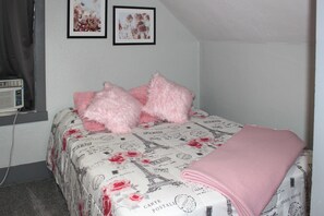 A bedroom with a bed, a pink blanket, and two framed pictures on the wall.