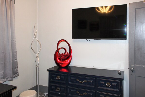 A room with a black dresser, a red vase, a flat-screen TV on the wall, and a curtain on the left.
