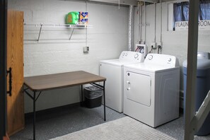 A laundry room with a washing machine, dryer, and a table with a trash bin.