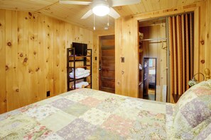 Ein Zimmer mit Holzboden, einem Bett, einem Fernseher auf einem Regal und einer Tür zu einem weiteren Raum.