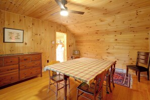 Ein Holzinterieur mit einem Esstisch, Stühlen, einer Holzkommode und einem Deckenventilator.