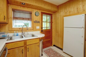 Eine Küche mit Holzwänden, einer Spüle, einem Kühlschrank und einem Fenster mit Jalousien.