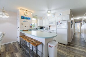 A modern kitchen with a central island, bar stools, a ceiling fan, and a view of the beach through the window. - Bayside Ocean City Condo w/ Water Views & Deck! (Ocean City)