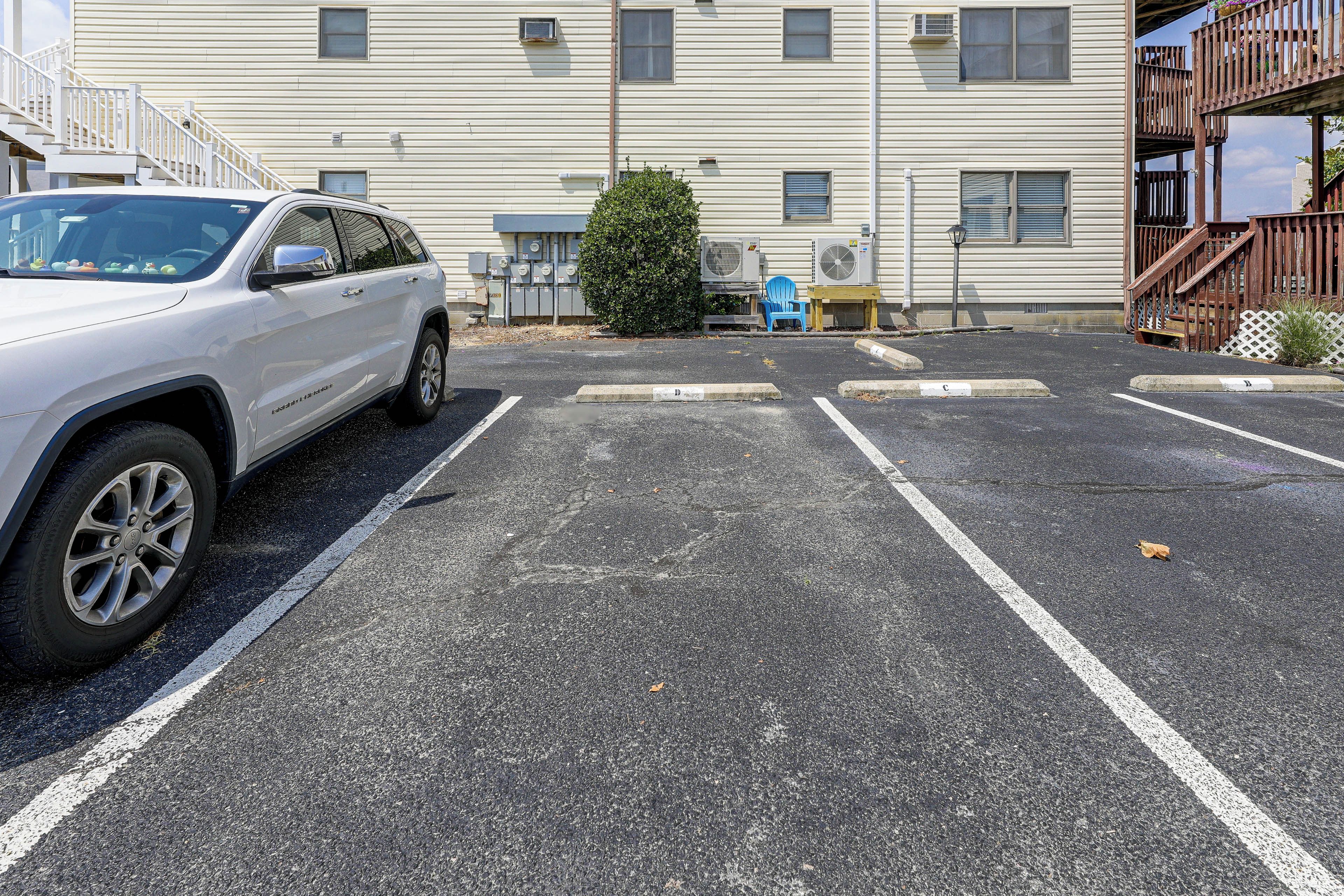 Un parcheggio con un SUV bianco parcheggiato in uno spazio. Si notano diverse unità di condizionamento d'aria montate sull'edificio sullo sfondo.