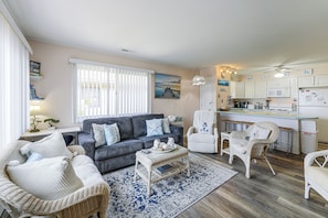 A cozy living room with a grey sofa, white armchairs, a coffee table, and a kitchen area with a microwave and refrigerator. - Bayside Waterfront OC Sleeps 8 | Beach | Boardwalk (Ocean City)