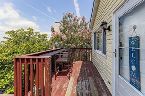 A wooden deck with outdoor furniture, a welcome sign, and a view of a pink flowering tree. - Bayside Waterfront OC Sleeps 8 | Beach | Boardwalk (Ocean City)
